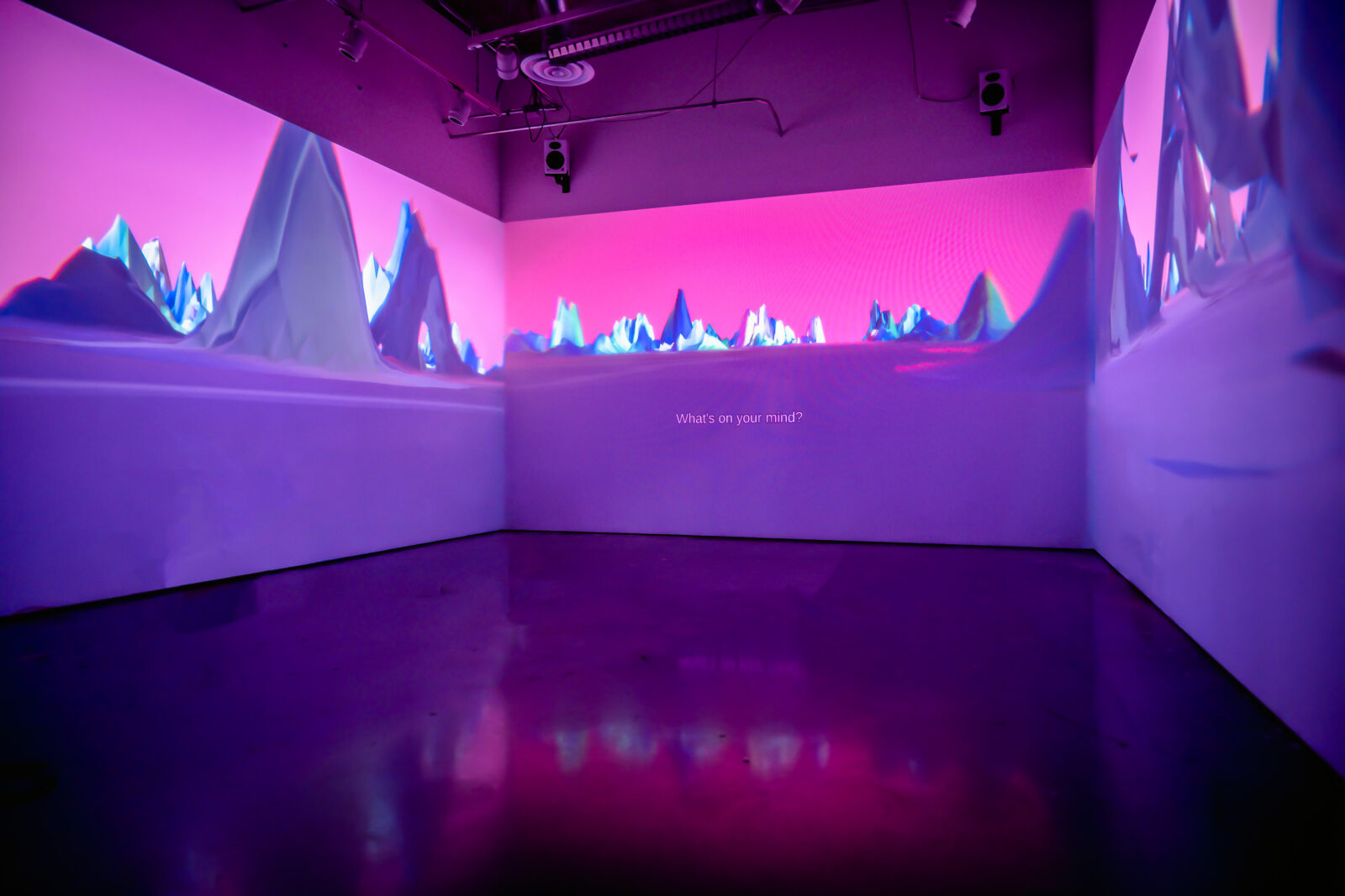 Three walls in a gallery with projections on them. The projections depict a pink sky and abstract purple mountains.
