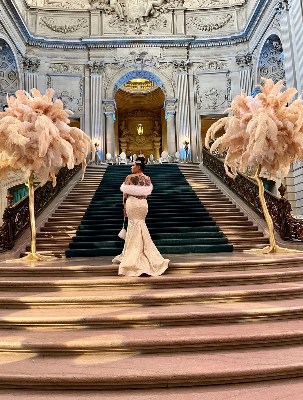 Rose Eden poses on a staircase in a white gown facing away from the camera