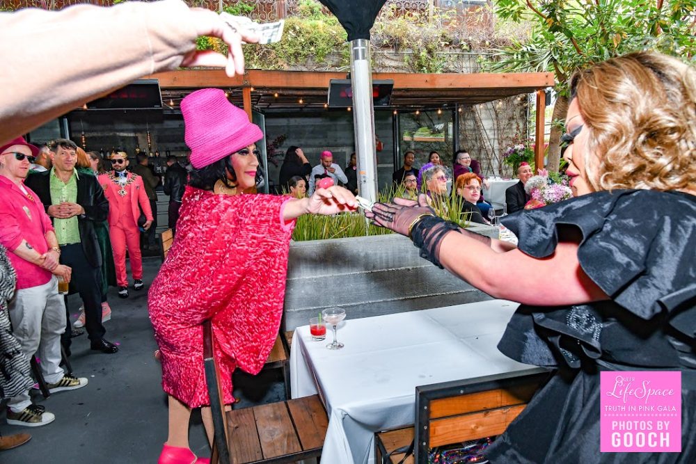 a drag queen tipping another performing drag queen