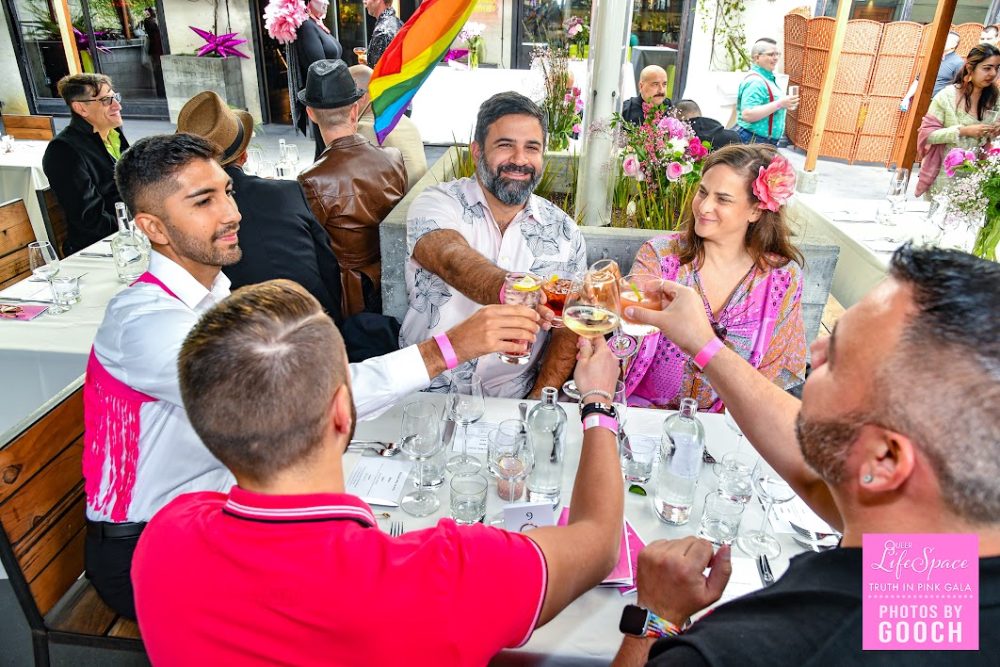 5 queers toast each other at their table