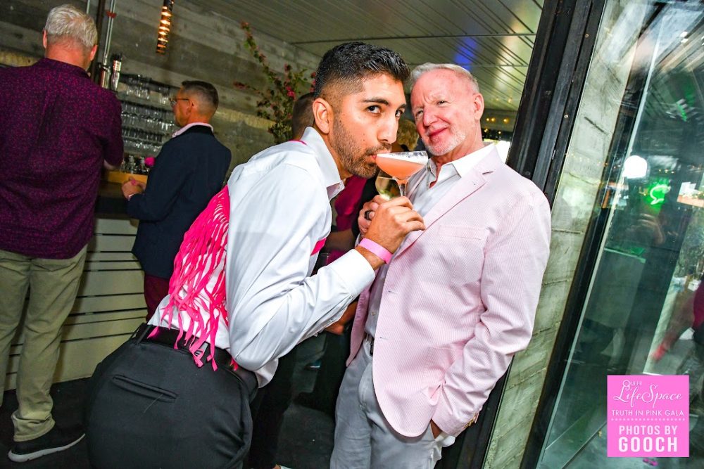 2 queers, one sipping a drink with a haughty expression