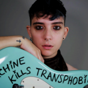 headshot of the artist holding a guitar with "this machine kills transphobia" written on it in black marker