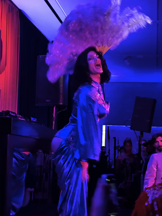 A drag performer laughs holding feather fans