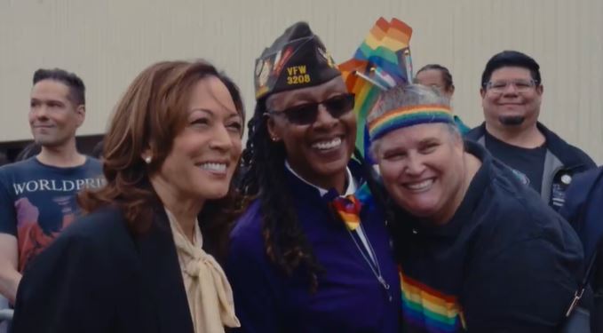 Kamala Harris taking a picture with a Black woman veteran hugging another woman, surrounded by rainbow flags.