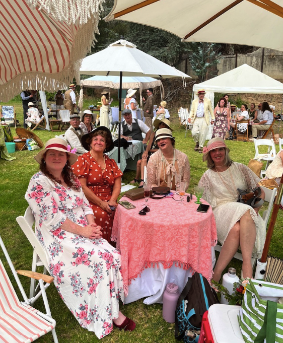 a group seated at a table beneath umbrellas on the lawn