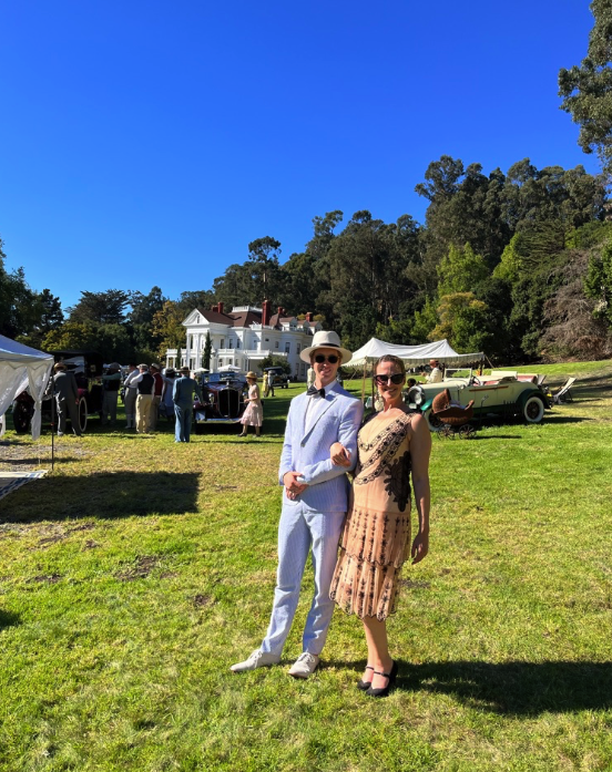 a couple pose on the lawn with the mansion in the distant background