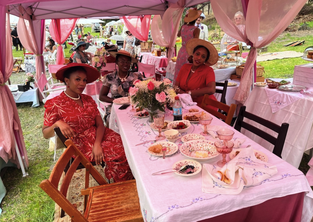 a group of Black women all dressed in red and pink pose beneath a matching canopy and table scape
