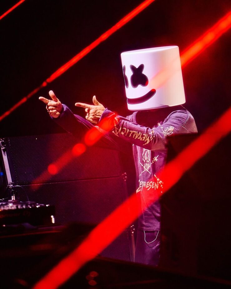 Marshmallow performing amidst red laser lights pointing 2 gun fingers in front of him