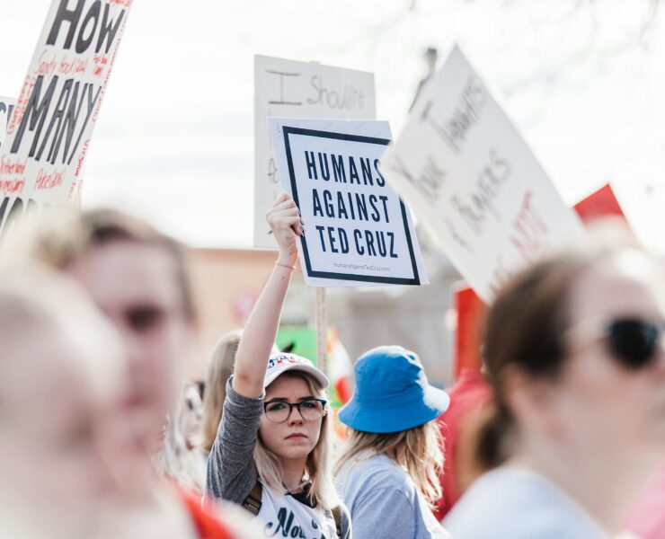 Colin Allred Destroys Ted Cruz in Senate Debate: Image of a protestor holding up a sign that says "humans against ted cruz" standing in the middle of a blurry crowd