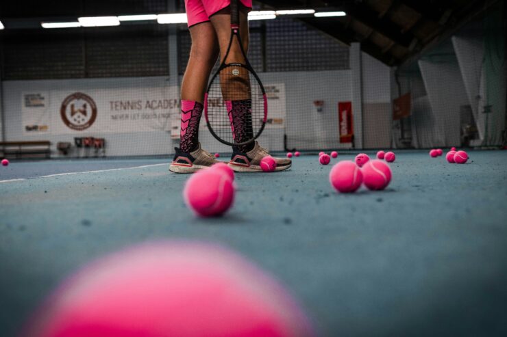 A trans girl stands on a tennis court surrounded by pink tennis balls.