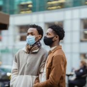 A queer black couple stands in the streets with masks on, preparing for changes to LGBTQ+ healthcare and access under a Trump administration.