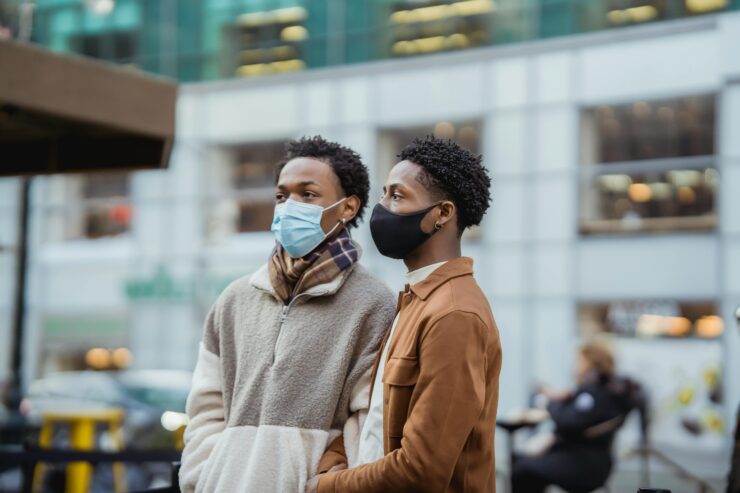 A queer black couple stands in the streets with masks on, preparing for changes to LGBTQ+ healthcare and access under a Trump administration.