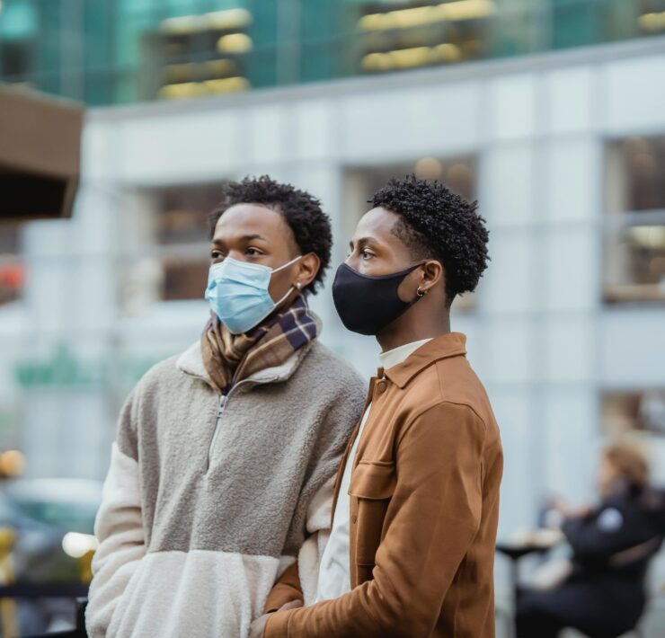 A queer black couple stands in the streets with masks on, preparing for changes to LGBTQ+ healthcare and access under a Trump administration.