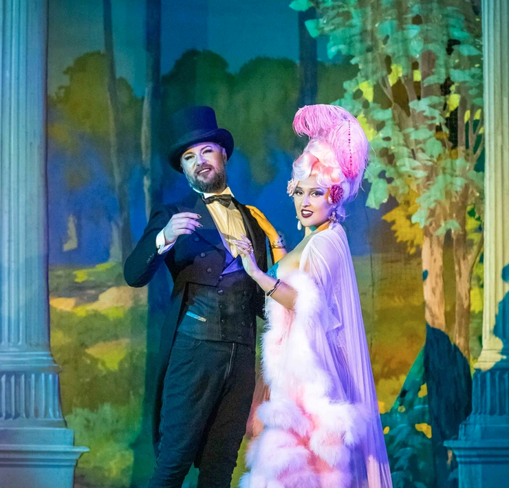 two performers wearing elaborate tuxedo and pink feathered outfits onstage