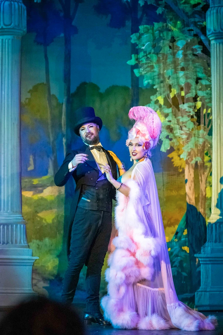 two performers wearing elaborate tuxedo and pink feathered outfits onstage