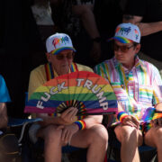 A closeup on the crowd watching the parade. One individual holds a rainbow fan that says Fuck Trump on it.